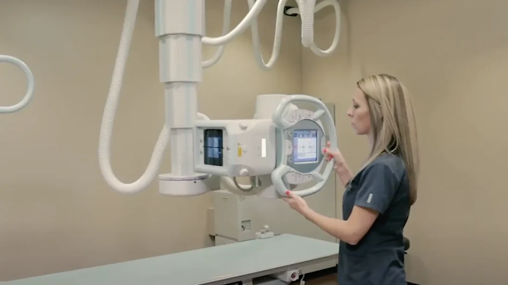 Technologist adjusting the control panel of a Shimadzu RADspeed Pro X-ray system in an exam room