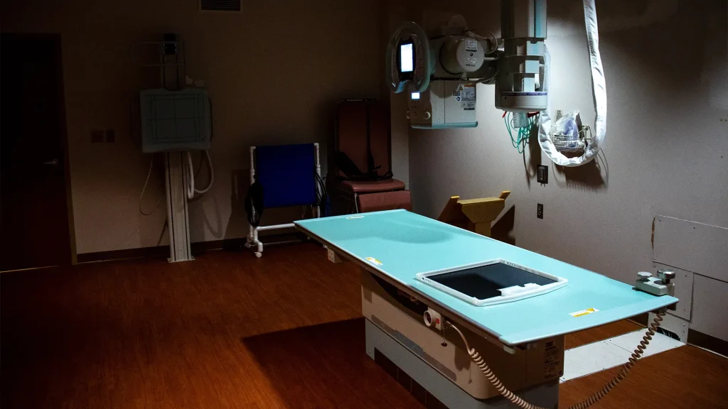 Dimly lit X-ray exam room at Boone County Hospital showing a wall-mounted detector and imaging table during a Shimadzu RADspeed Pro installation