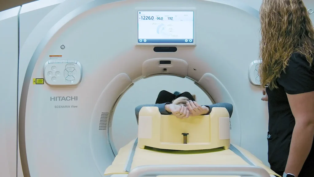 Patient entering a Hitachi Scenaria View CT scanner headfirst while a technologist looks on