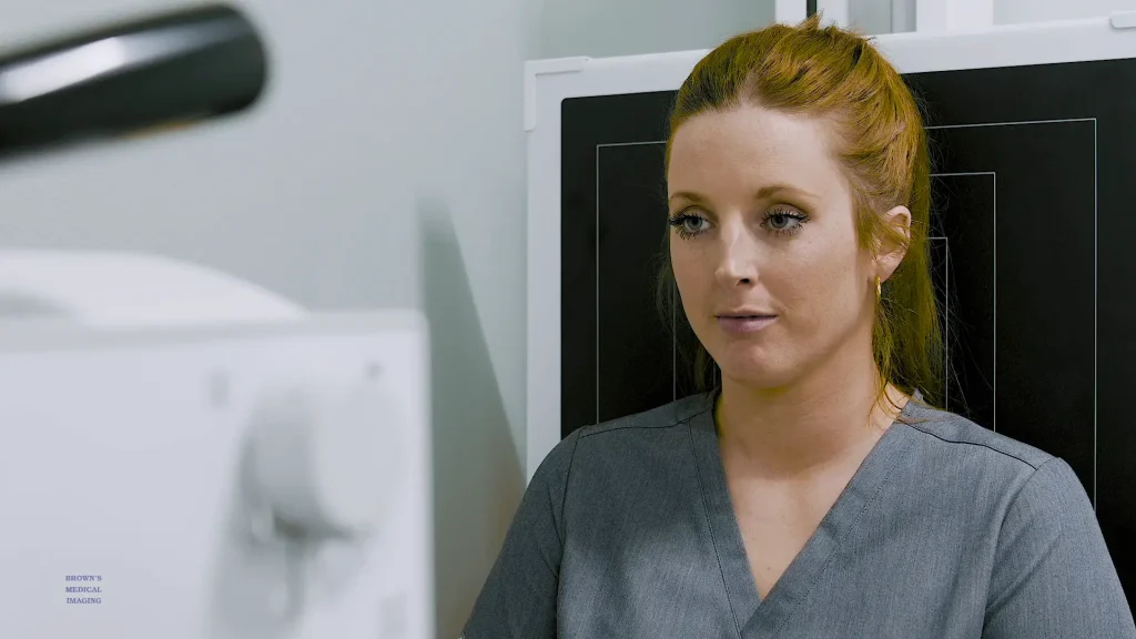 Woman in scrubs speaking on camera in an X-ray exam room, testimonial video still