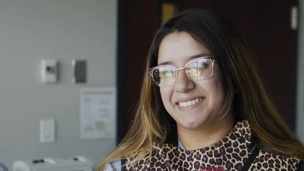 Smiling radiography student wearing a leopard-print lead apron in a clinical setting, testimonial video still