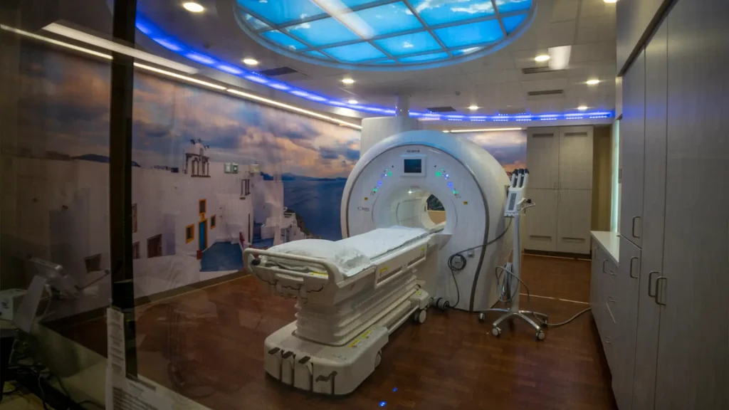 MRI exam room with a scenic wall mural, blue ceiling skylight graphic, and a scanner with patient table