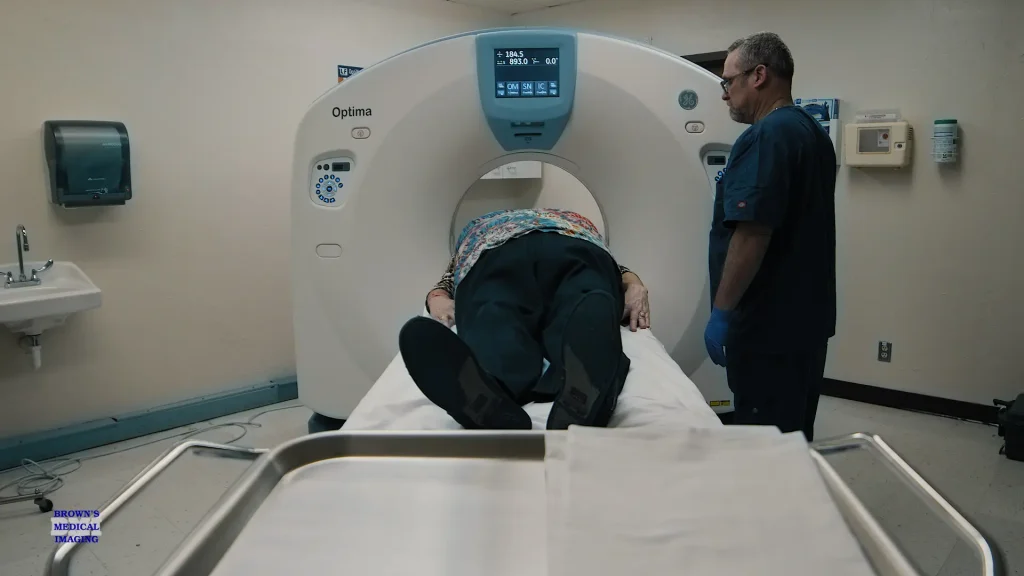 Technologist assisting a patient into the bore of a GE Optima CT scanner