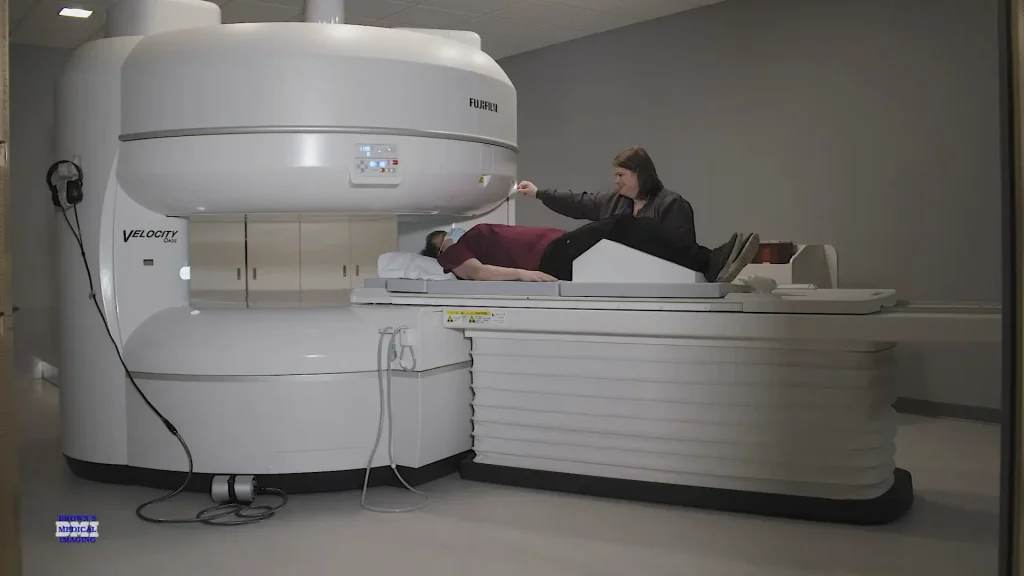 Technologist assisting a patient onto the table of a Fujifilm Velocity open MRI scanner