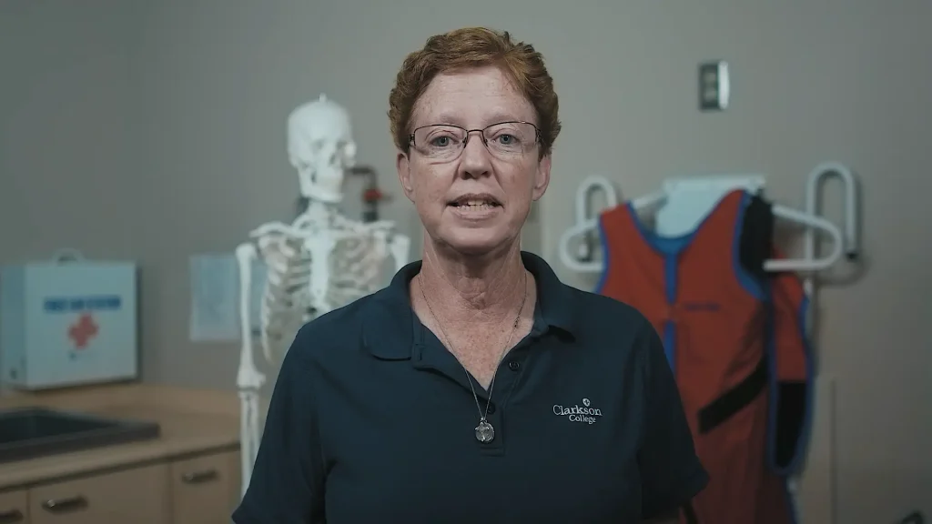 Clarkson College radiologic technology instructor standing in an exam room with an anatomical skeleton model in the background