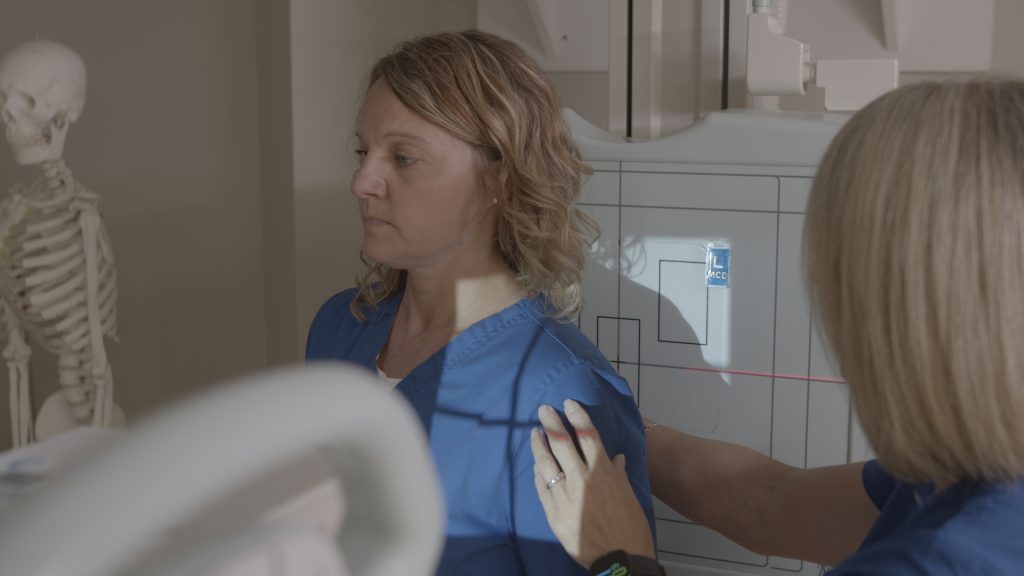 Technologist positioning a patient's shoulder against an X-ray detector panel for a scapular Y view