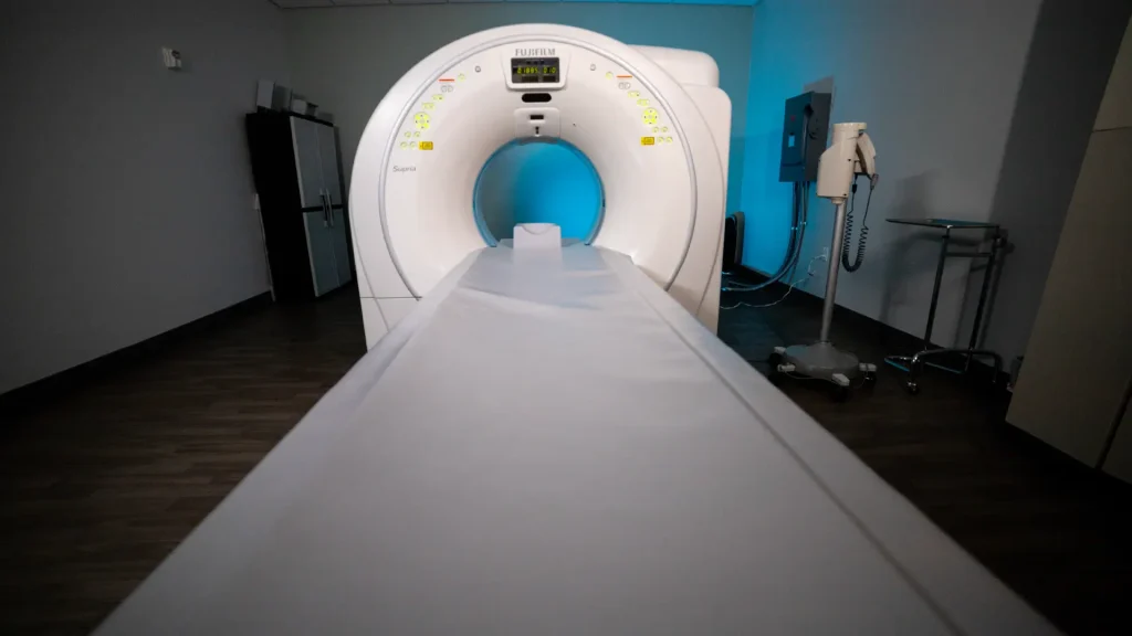 Fujifilm Supria CT scanner with illuminated blue bore opening in a dimly lit exam room