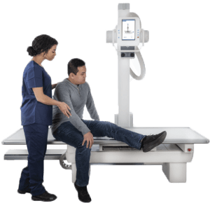 Technologist assisting a seated patient onto the Acuity FDR+ exam table for positioning