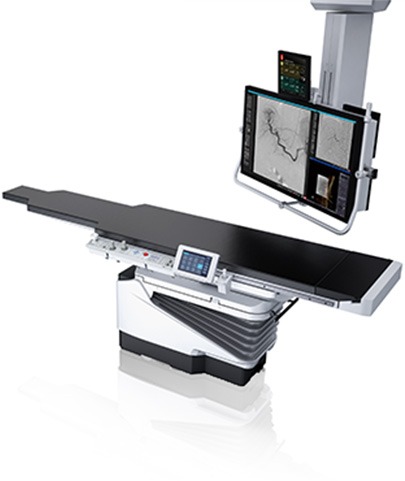 Canon Trinias interventional imaging system showing the C-arm, exam table, and dual display monitors with angiographic images