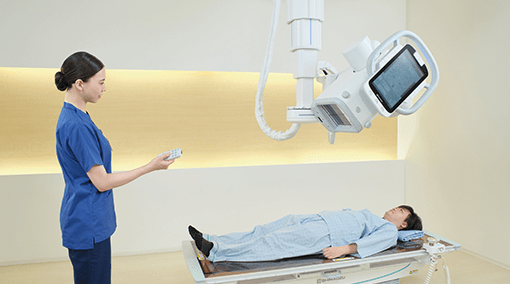 Technologist using a wireless remote to operate the overhead tube unit while a patient lies on the RADspeed Pro SR5 table
