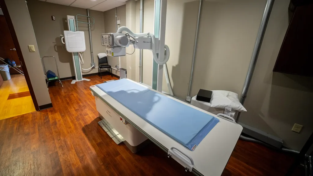 Wall-mounted digital X-ray system with overhead tube and exam table in an orthopedic department room