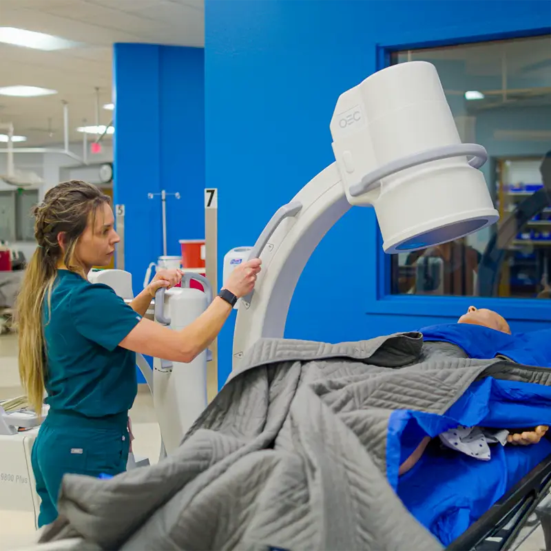 Clinician in scrubs positioning an OEC mobile C-arm over a draped patient in an operating room