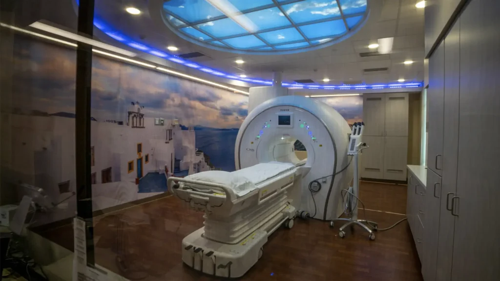 MRI exam room with a scenic wall mural, ceiling skylight graphic, and a CT/MRI scanner with patient table