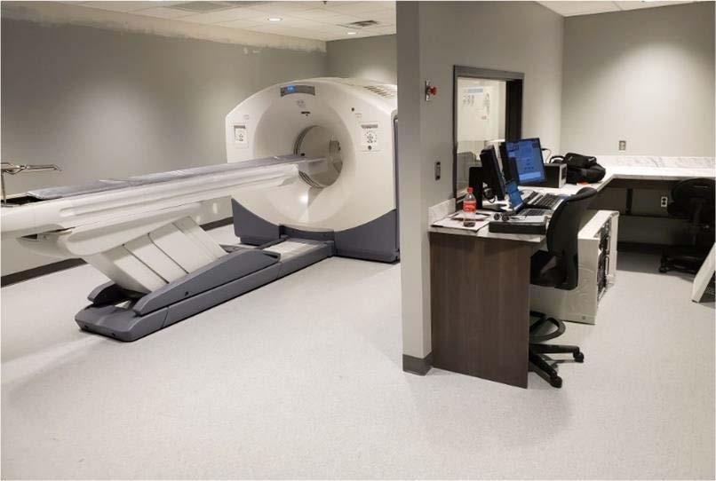 CT scanner suite with patient table extended into the gantry, next to a technologist workstation