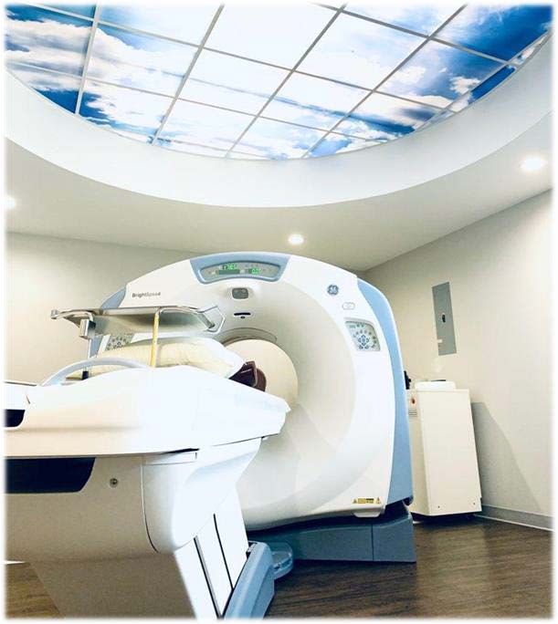 GE BrightSpeed CT scanner with patient table extended, in a room with a sky-mural ceiling
