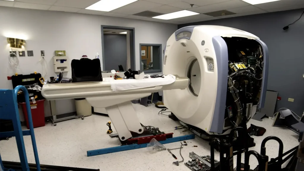 Technicians reconditioning a Hitachi CT scanner with the gantry cover open, exposing internal components