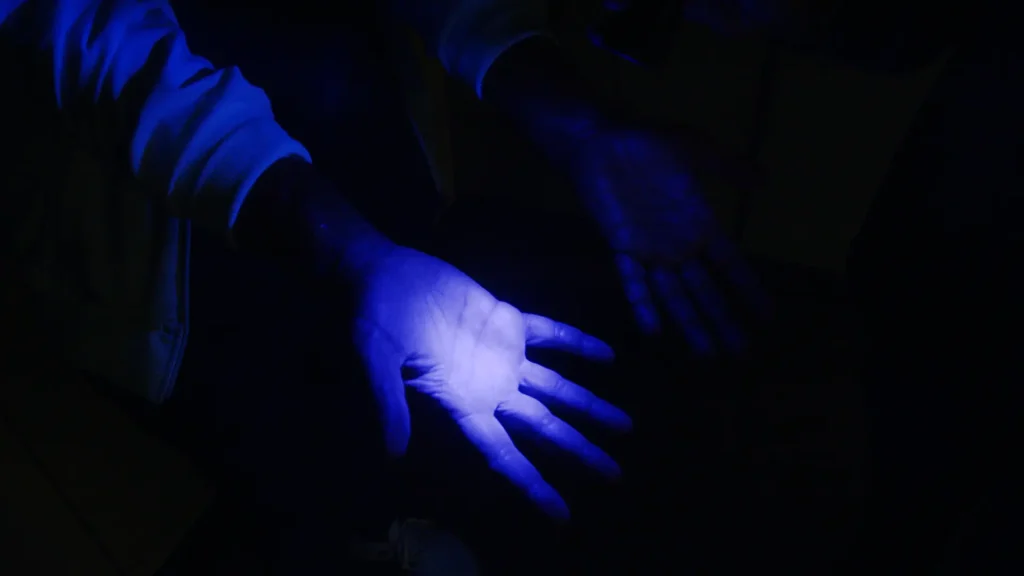 Close-up of hands under blue ultraviolet light demonstrating handwashing technique