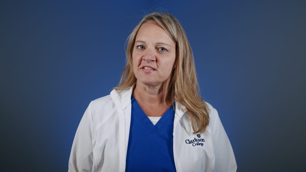 Portrait of a Clarkson College imaging student in a white lab coat and blue scrubs speaking against a blue background