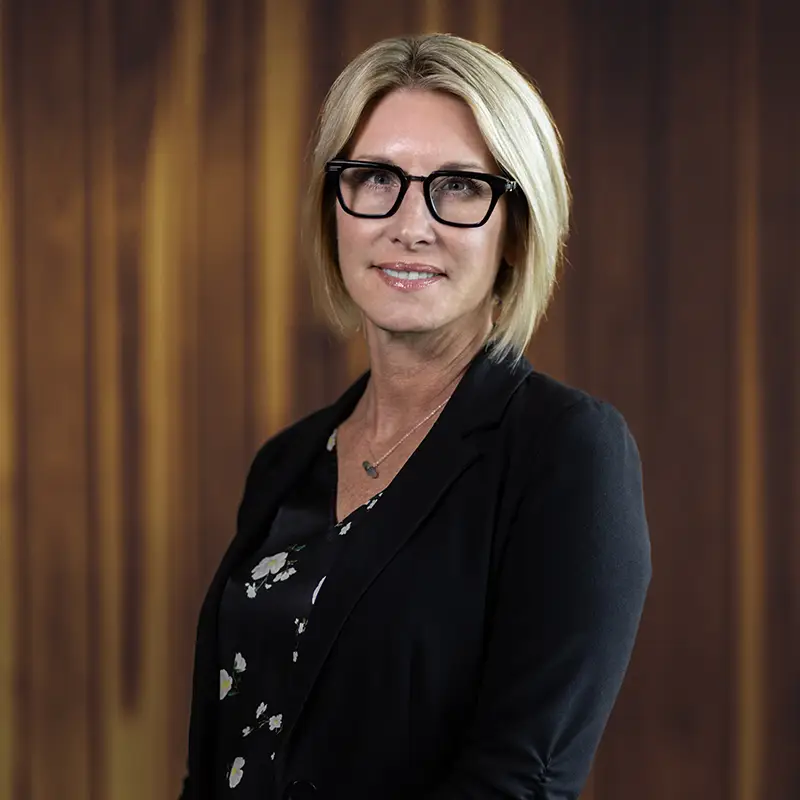 Professional headshot of a woman with blonde hair and glasses wearing a black blazer