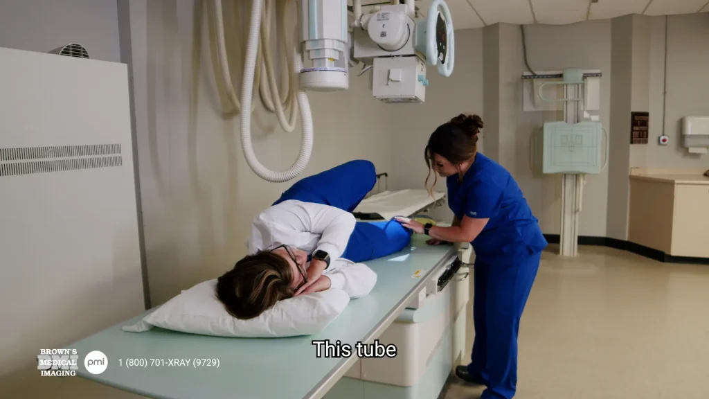 Technologist positioning a patient's leg on an X-ray table for a lateral knee X-ray, with captioning text reading 'This tube'