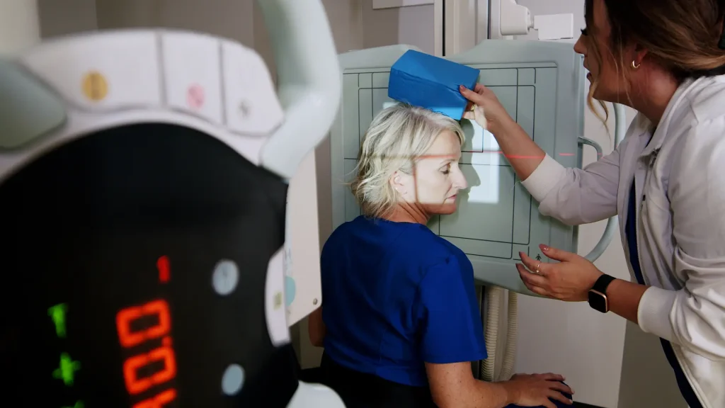 Technologist positioning a patient's head against a digital X-ray detector panel using foam positioning blocks for a lateral head X-ray