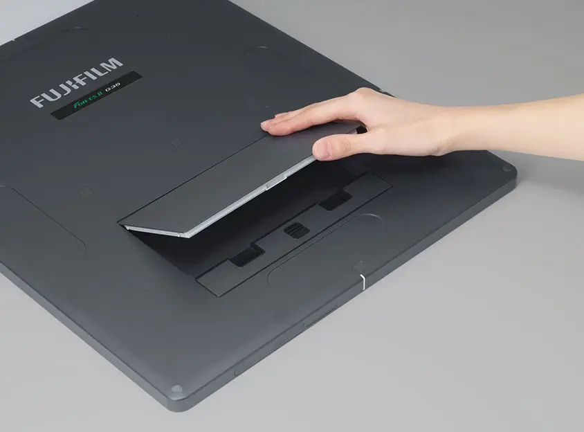 Hand replacing the battery on the underside of a Fujifilm FDR ES II detector panel