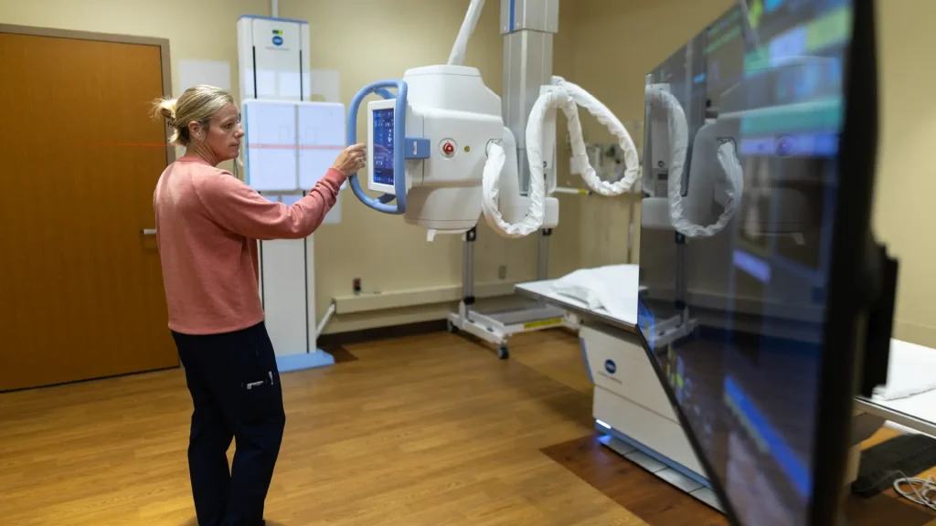 Technologist adjusting the overhead tube crane controls of a Konica Minolta KDR Flex X-ray system in an exam room