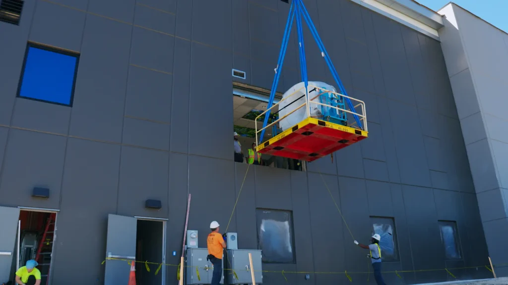 CT scanner component being hoisted through a second-story building window using a crane and rigging