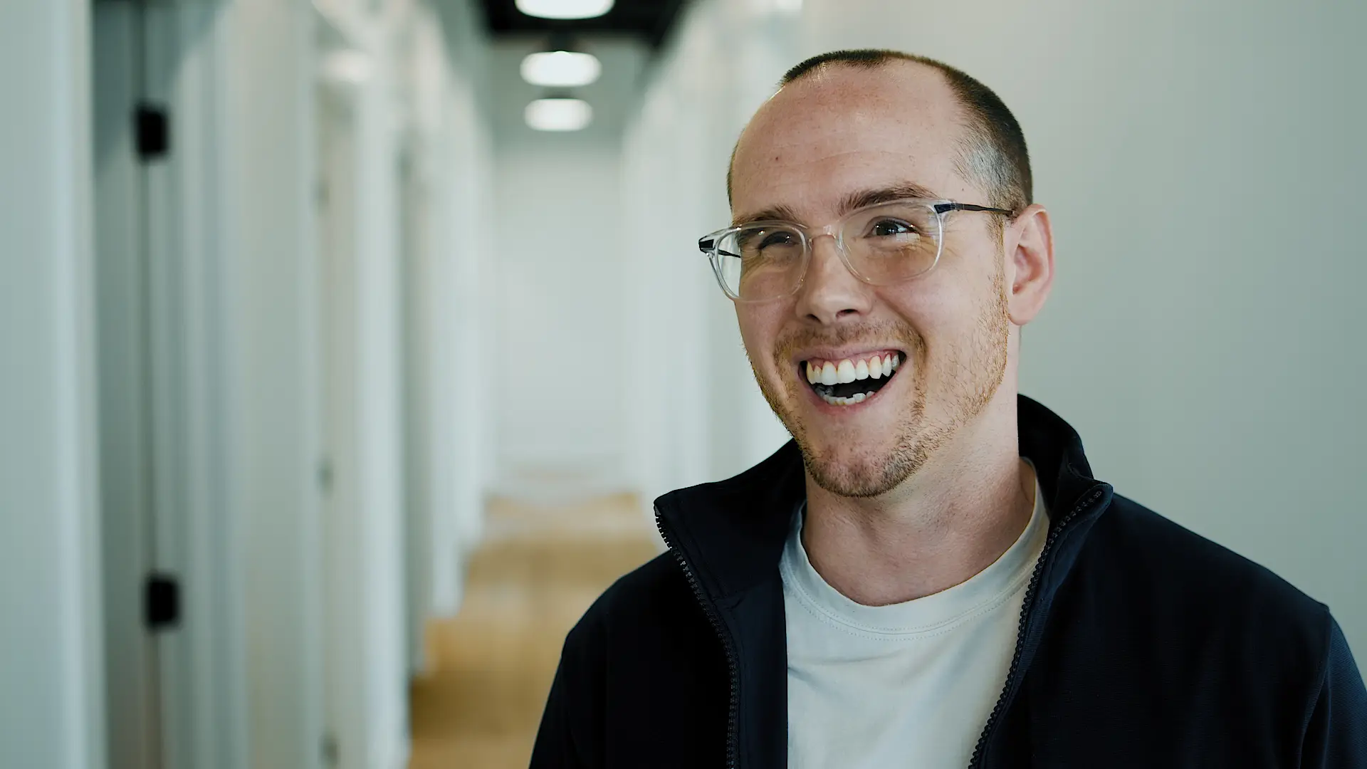 Smiling man with glasses in a hallway giving a video testimonial