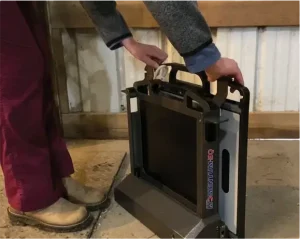 Close-up of hands operating a Momentum DR portable X-ray generator in a barn setting