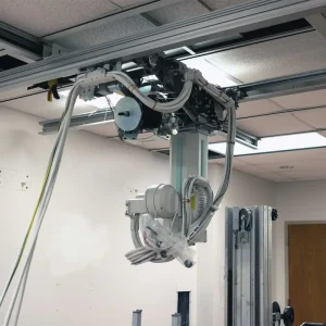 Ceiling-mounted X-ray tube assembly being serviced, suspended from overhead rail tracks with cables wrapped in protective plastic