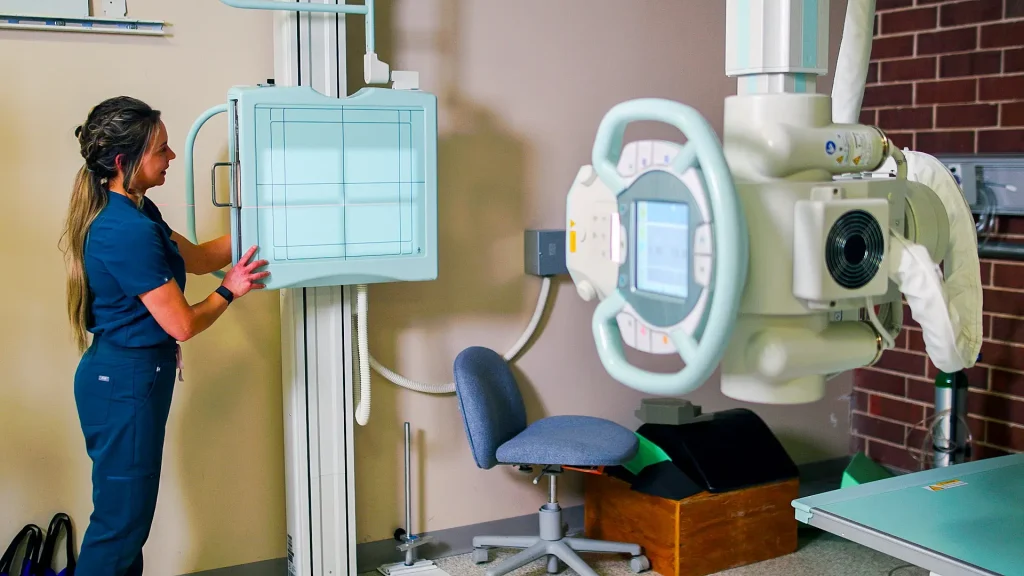 Technologist positioning a wall-mounted digital X-ray detector panel next to a mobile X-ray generator