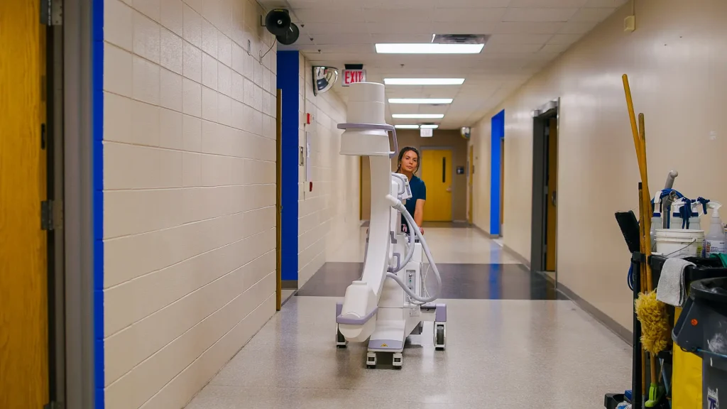 Technologist pushing a mobile X-ray unit down a hospital hallway