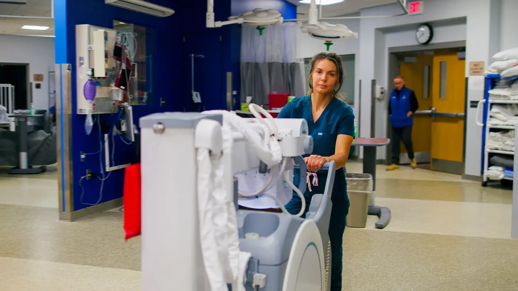 Technologist pushing a mobile X-ray unit down a hallway in a clinical training facility